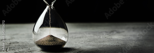 Hourglass on a dark background, long banner. Urgency and running out of time concept