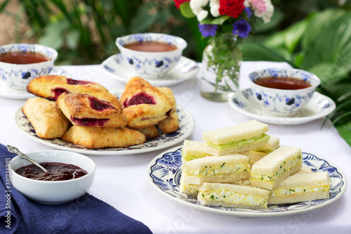 Photography Afternoon tea in the garden with scones, strawberry jam, finger sandwiches with cucumber and egg salad