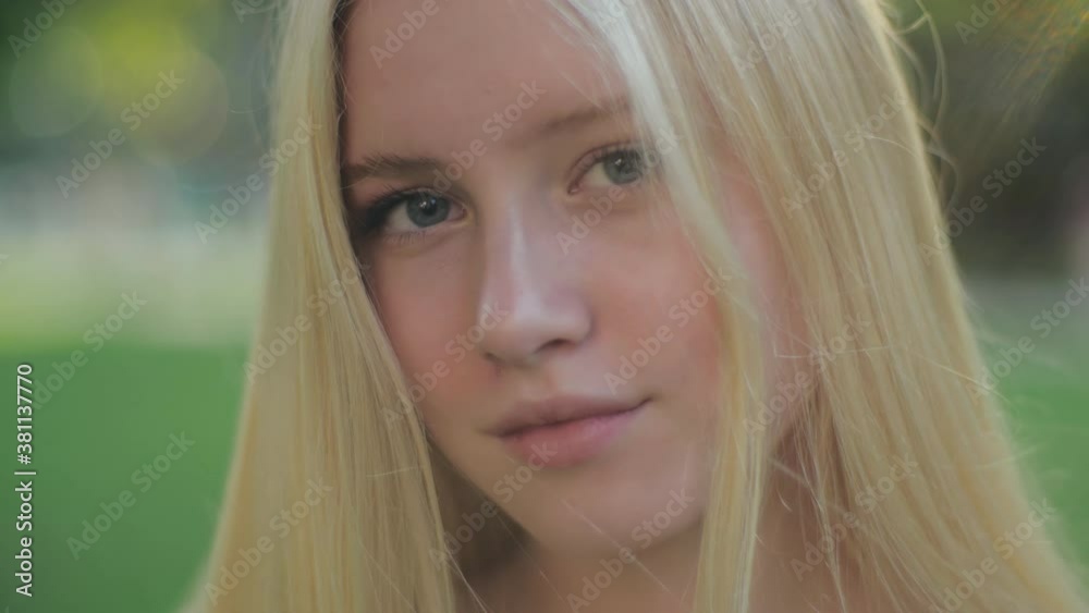 Close-up portrait of a beautiful Caucasian girl with blue eyes, no makeup, with blond hair, smiling sweetly and looking at the camera at sunset. The concept of aesthetics and health.