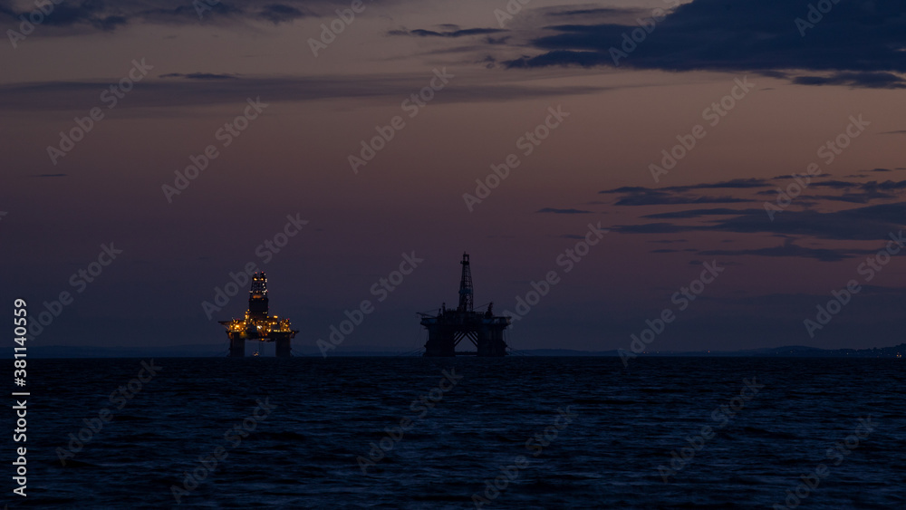 Oil rigs of the coast of Scotland, illuminated by their lights as the sun sets Oil rigs of the coast of Scotland, illuminated by their lights as the sun sets