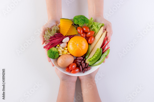 Woman hand giving the plate of  fresh vegetables, fruit, herbs and spices to child. World food day or Charity concept.