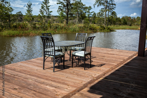 A set of black metal chairs and a table sitting on a large wooden dock deck outside of a hunting and fishing cabin near a large pond in Georgia for outdoor dining