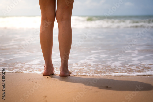 Close-up at woman foot and heel part that standing on the beach front. Holiday and vacation at the sea concept. Photo applied with sun shade lighting - high brightness.