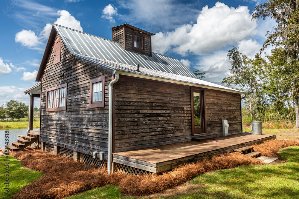 Scenic view of the rear exterior of a rural rustic wooden camp house used for fishing and hunting. The house is located on a large pond Scenic view of the rear exterior of a rural rustic wooden camp house used for fishing and hunting. The house is located on a large pond