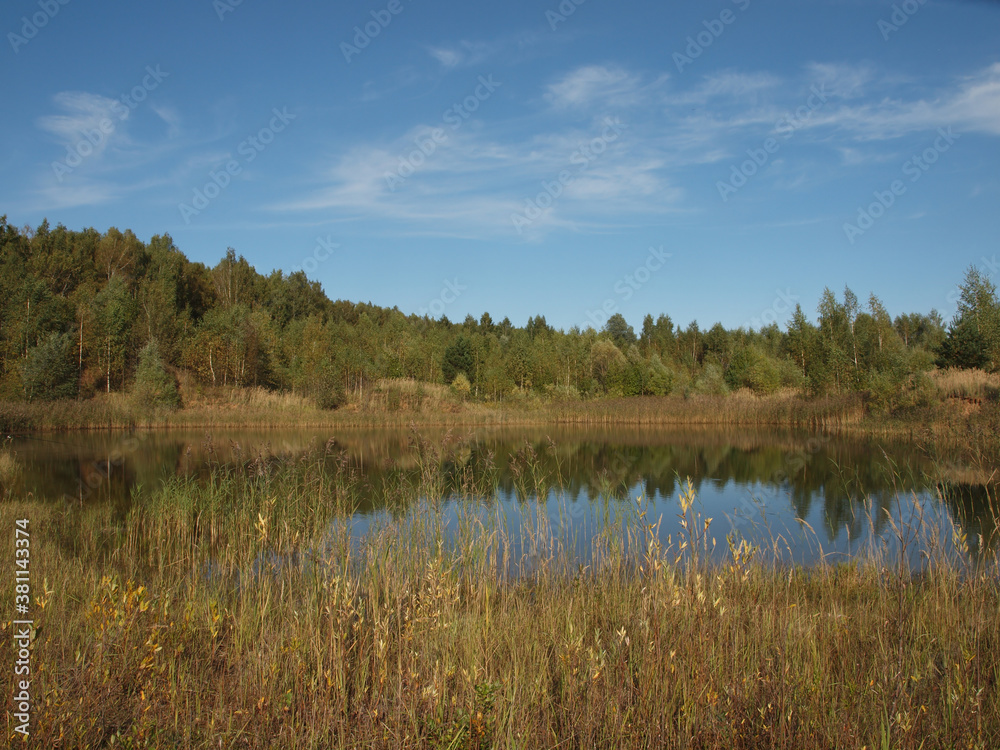Autumn landscape. Autumn sky and forest reflected in the water surface of the pond.