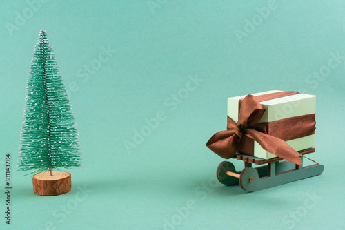 The gift lies on the sleigh next to the Christmas tree on turquoise background . christmas concept. postcard.