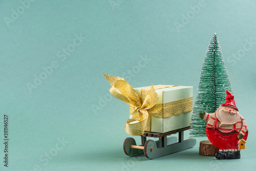 The gift lies on the sleigh next to the Christmas tree and Santa Claus on turquoise background . christmas concept. postcard.