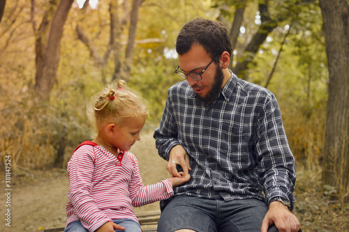 Baby and father are playing in the autumn park. Dad and daughter are sitting on a wooden bridge outdoors. Happy family moments of childhood.