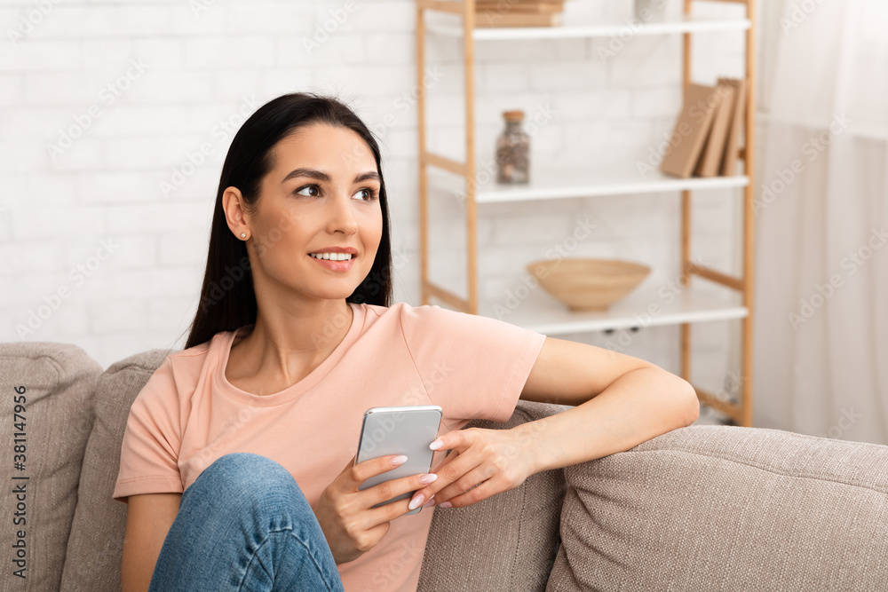 Distracted woman holding mobile phone sitting on the couch Distracted woman holding mobile phone sitting on the couch
