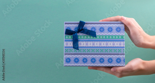 Female hands holding blue gift box decorated with blue ribbon on turquoise background.christmas concept. copy spase