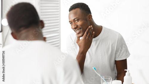 African American Man Touching Face After Shaving Standing In Bathroom