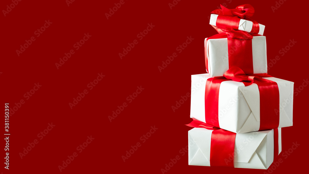 Christmas gifts. Greeting surprise. Happy New Year 2021. Festive celebration. Stacked present boxes in white wrapped paper taped ruby ribbon isolated on red copy space.