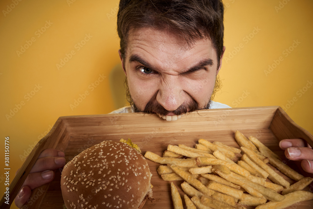 Man with wooden pallet fast food hamburger french fries diet food intake close-up Man with wooden pallet fast food hamburger french fries diet food intake close-up
