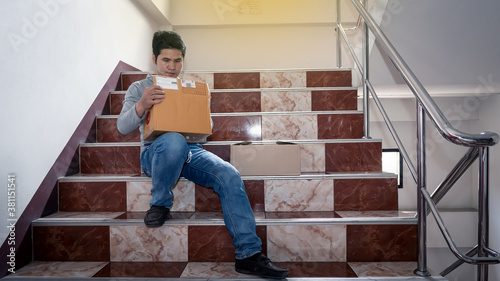 An Asian man sitting on the stairs holding a cardboard box from an online purchase.