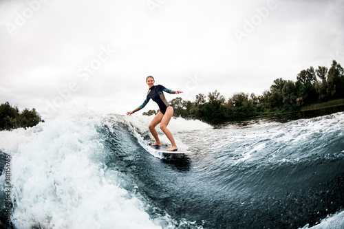 Cheerful woman in wetsuit rides down on surf style wakeboard on wave