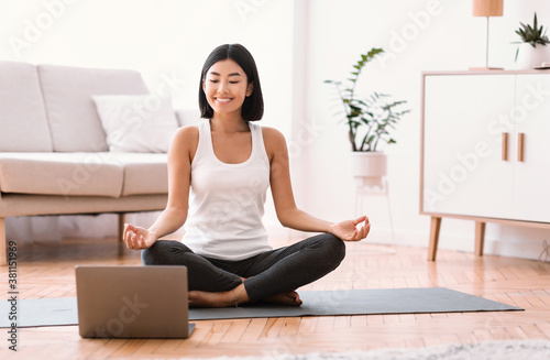 Millennial woman meditating with trainer online on laptop