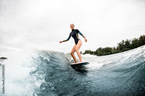 sportive woman standing on surf style wakeboard and rides the wave.