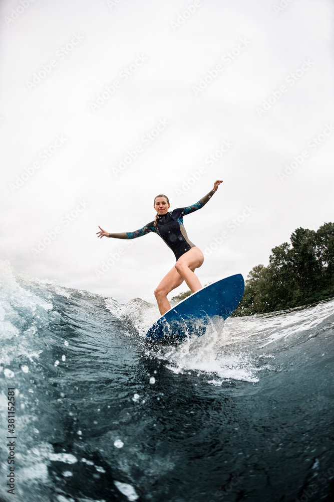 Active woman stands with bent knees on surfboard and ride on wave
