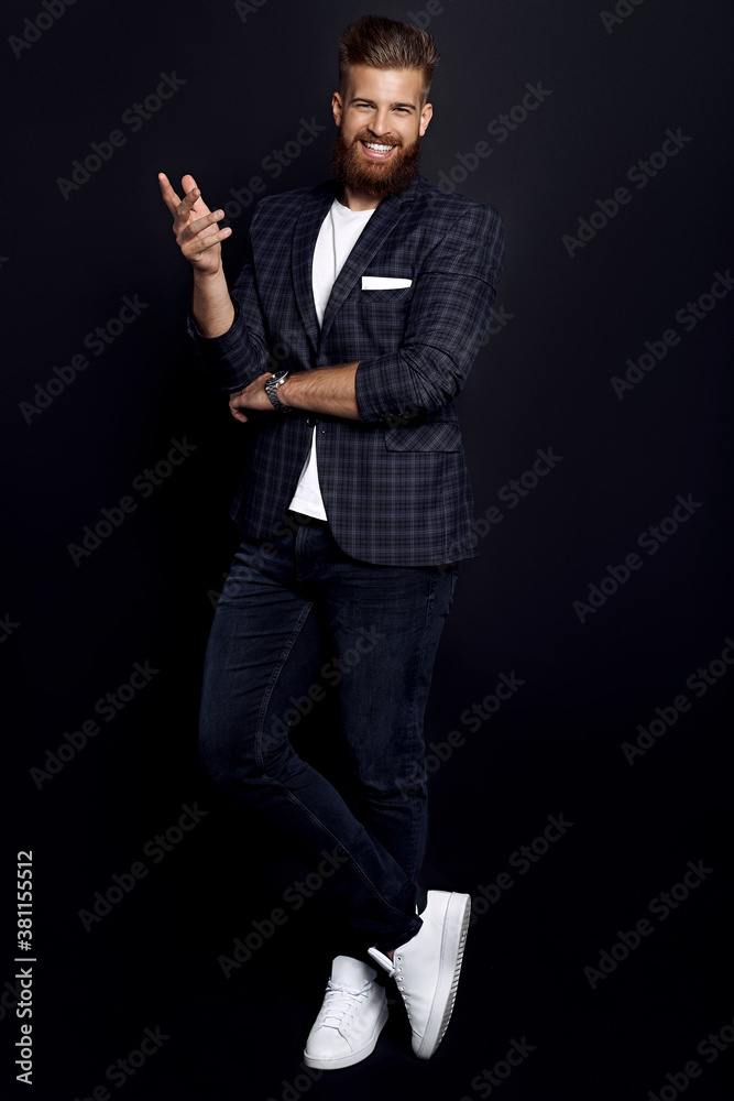 Confident and handsome. Full length of young man with ginger beard in smart-casual clothes smiling looking at camera while posing against black background