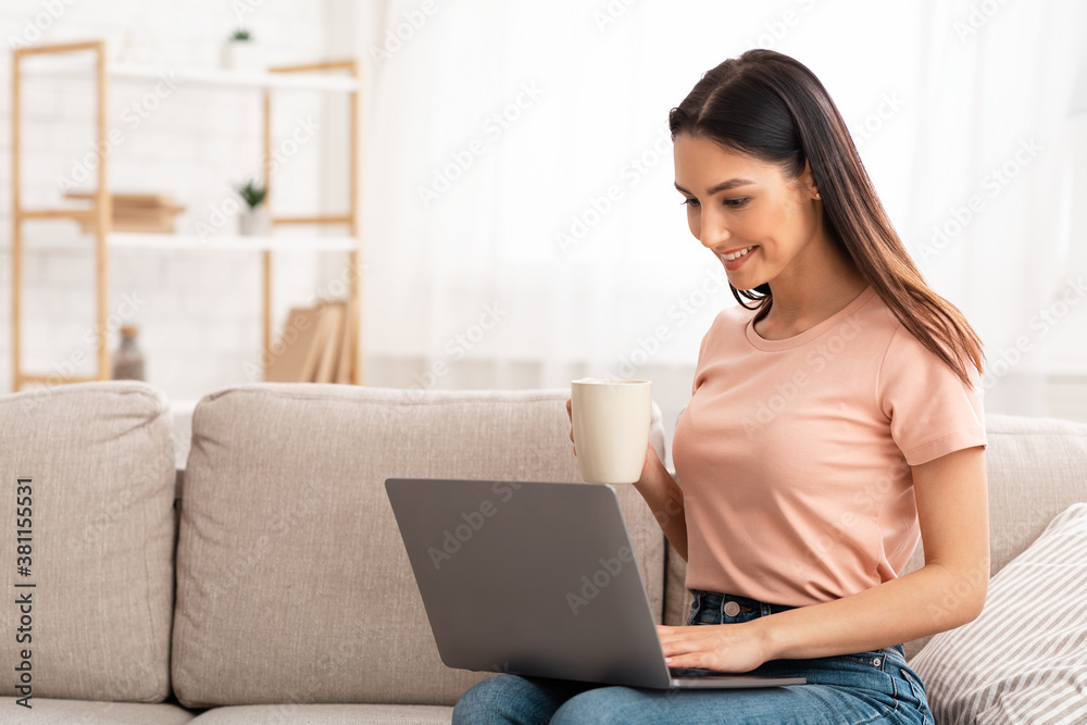 Woman using laptop phone sitting on sofa, drinking coffee Woman using laptop phone sitting on sofa, drinking coffee
