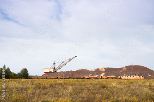 A large walking excavator forms dumps of rock delivered by freight train from a mining quarry. Background © Roman