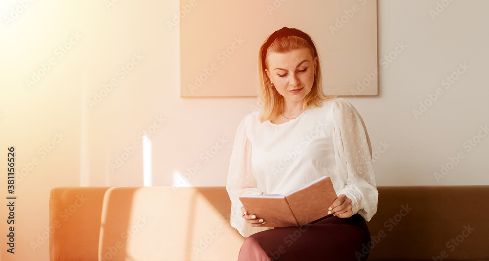 Indoor shot of trendy looking young woman sitting on a comfortable sofa in living room and writing down in diary, making grocery list before going shopping Indoor shot of trendy looking young woman sitting on a comfortable sofa in living room and writing down in diary, making grocery list before going shopping