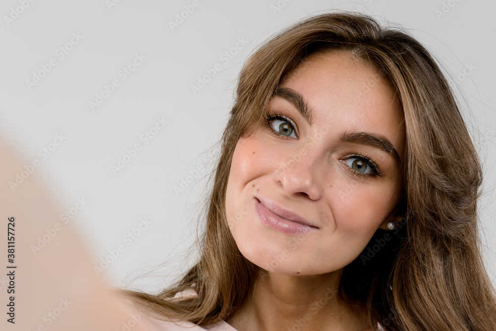 Happy moments must be saved. Cheerful young woman holding camera and making selfie while standing against grey background Happy moments must be saved. Cheerful young woman holding camera and making selfie while standing against grey background