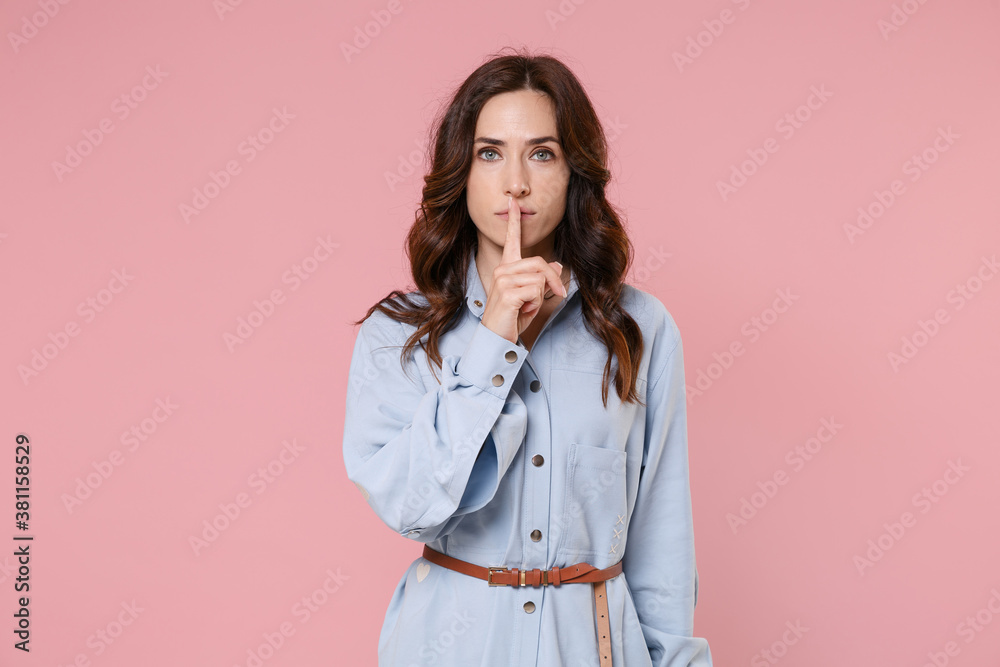 Secret young brunette woman 20s wearing casual blue shirt dress posing saying hush be quiet with finger on lips shhh gesture looking camera isolated on pastel pink colour background, studio portrait. Secret young brunette woman 20s wearing casual blue shirt dress posing saying hush be quiet with finger on lips shhh gesture looking camera isolated on pastel pink colour background, studio portrait.