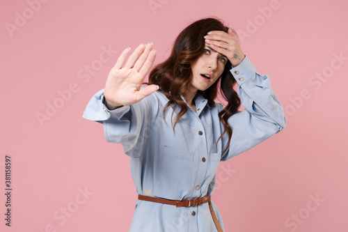 Worried displeased tired young brunette woman 20s in casual blue shirt dress showing stop gesture with palm put hand on head looking camera isolated on pastel pink colour background, studio portrait.