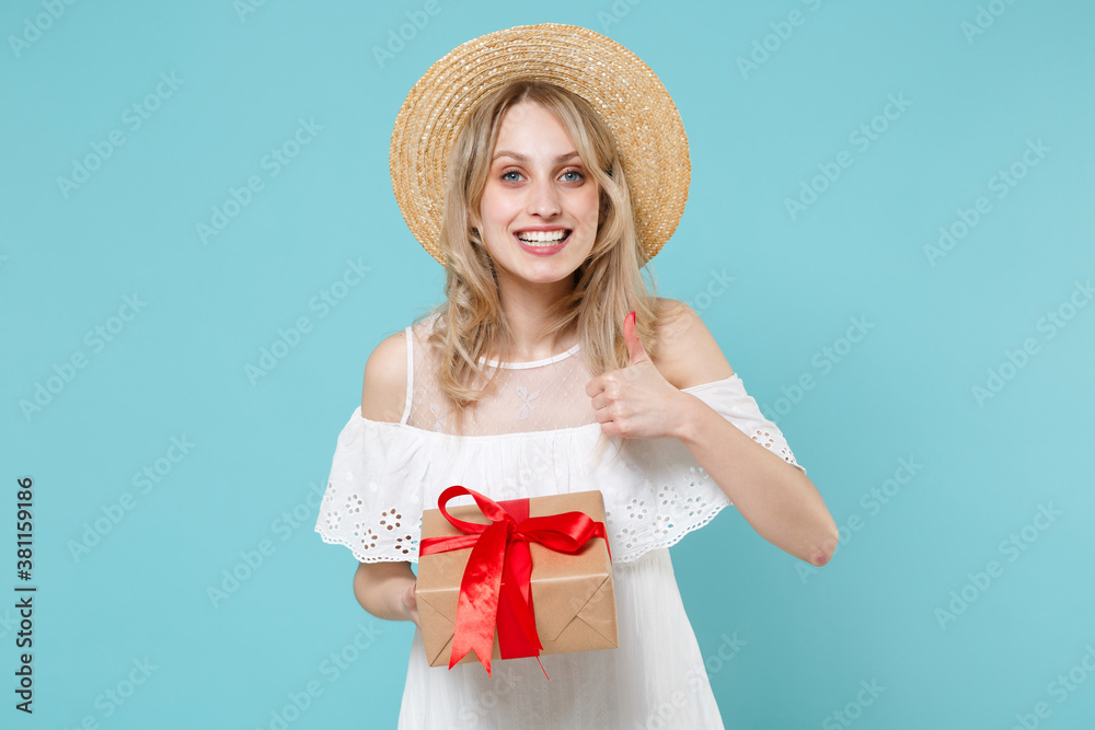 Smiling young woman in white summer dress hat hold red present box with gift ribbon bow showing thumb up isolated on blue turquoise background. Valentine's Day Women's Day birthday holiday concept. Smiling young woman in white summer dress hat hold red present box with gift ribbon bow showing thumb up isolated on blue turquoise background. Valentine's Day Women's Day birthday holiday concept.