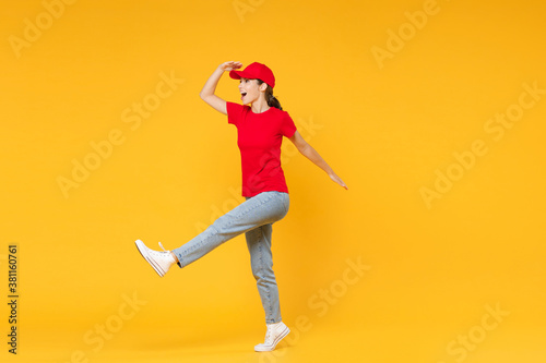 Full length body delivery employee woman in red cap blank t-shirt uniform work courier in service during quarantine coronavirus covid-19 virus standing isolated on yellow background studio portrait. © ViDi Studio