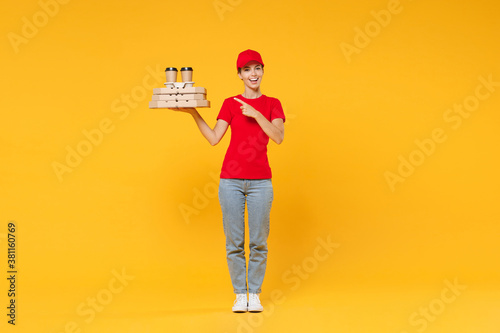 Full length body delivery employee woman in red cap blank t-shirt uniform work courier in service hold bring food order pizza in cardboard flatbox, paper cups of coffee isolated on yellow background.