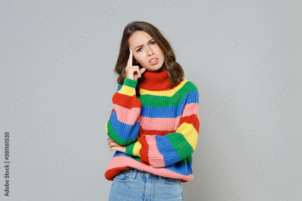 Preoccupied puzzled perplexed concerned young brunette woman 20s wearing casual colorful knitted sweater standing put hand on head looking camera isolated on grey colour background, studio portrait.