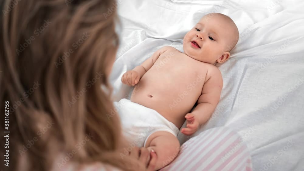 Cute baby in diaper lying on white sheet bed looking on mother. Shot on RED Raven 4k Cinema Camera Cute baby in diaper lying on white sheet bed looking on mother. Shot on RED Raven 4k Cinema Camera