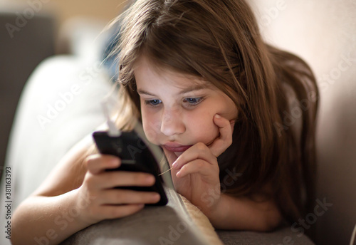 
the child lies on the couch and looks at the phone