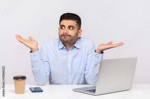 Don't know! Puzzled clueless confused businessman sitting office workplace with laptop on desk, shrugging shoulders, doubting can`t make decision. indoor studio shot isolated on white background