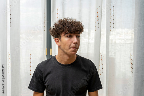 Attractive young man with curly hair wearing black t-shirt posing on white curtains background