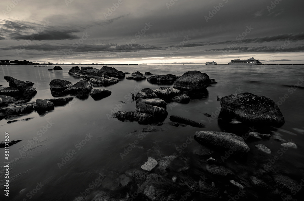 Finnish gulf at sunset with stones and 2 passenger ships in black and white