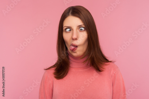 Closeup portrait of funny crazy woman crossing eyes and showing tongue, having fun making dumb face expression, fooling face. Indoor studio shot isolated on pink background