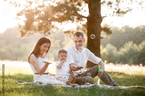 father, mother and son blow soap bubbles in the park together on a sunny summer day. happy family having fun outdoor