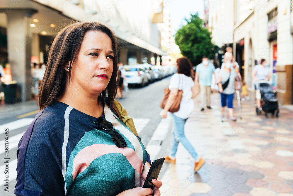 Moroccan brunette mature woman without a mask on a street in Europe looking straight ahead with a phone in her hands