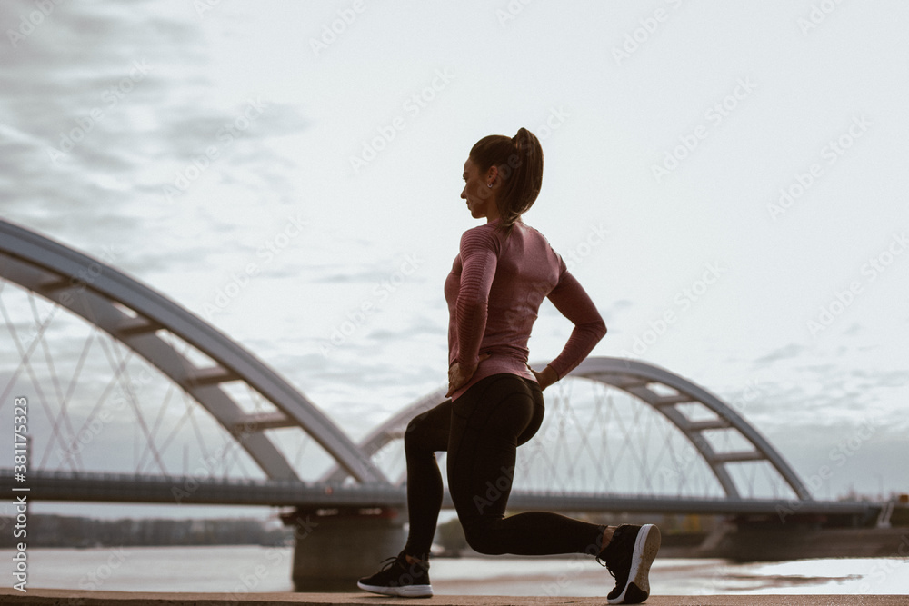 Beautiful young woman during the morning doing leg warm-up exercises, side view