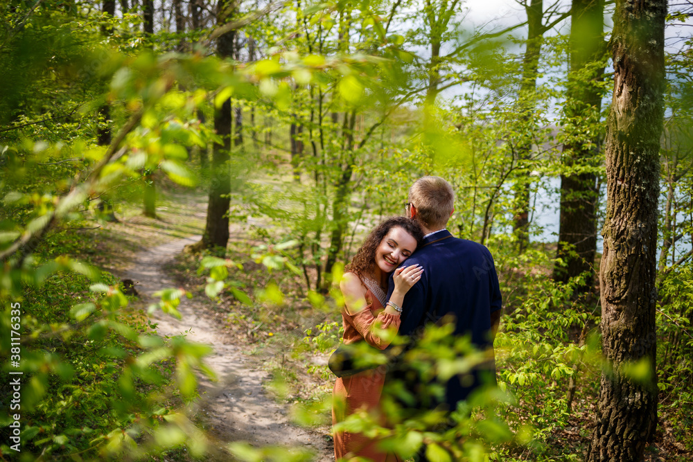 Romantic walk of a young couple in a green forest, warm spring weather. Guy and girl hugging in nature