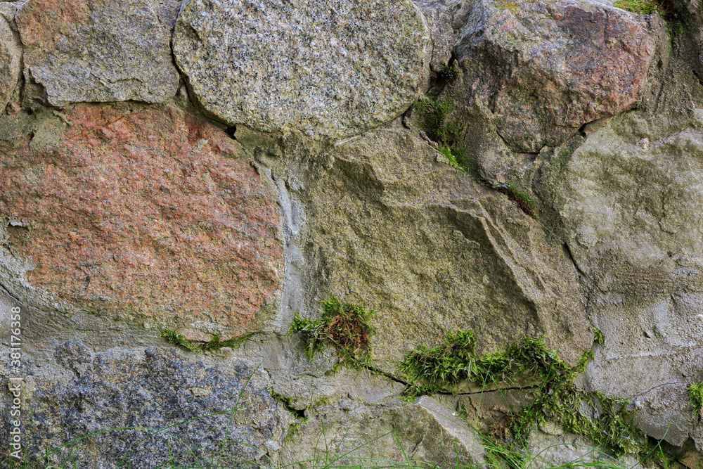 Fragment of a wall made of natural chipped stone covered with moss