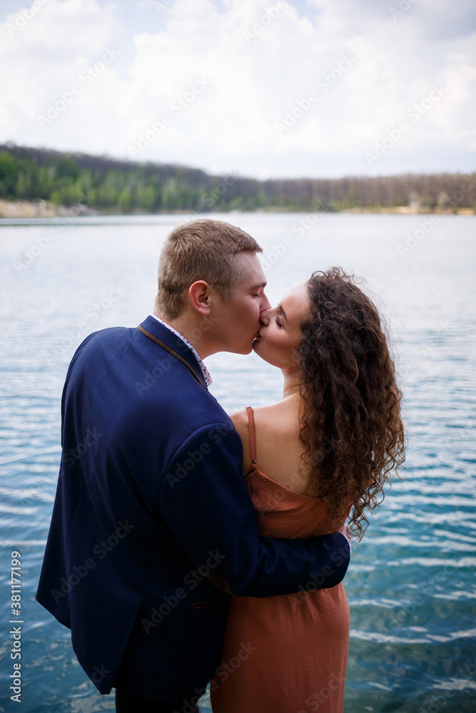 A young couple holding hands on a wooden bridge in the middle of a blue lake. Masonry on the island on a background of trees. Nature, landscape. Romance and love, happy couple A young couple holding hands on a wooden bridge in the middle of a blue lake. Masonry on the island on a background of trees. Nature, landscape. Romance and love, happy couple