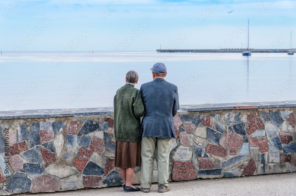 Older people, a man and a woman stand on the waterfront and look at the evening sea.