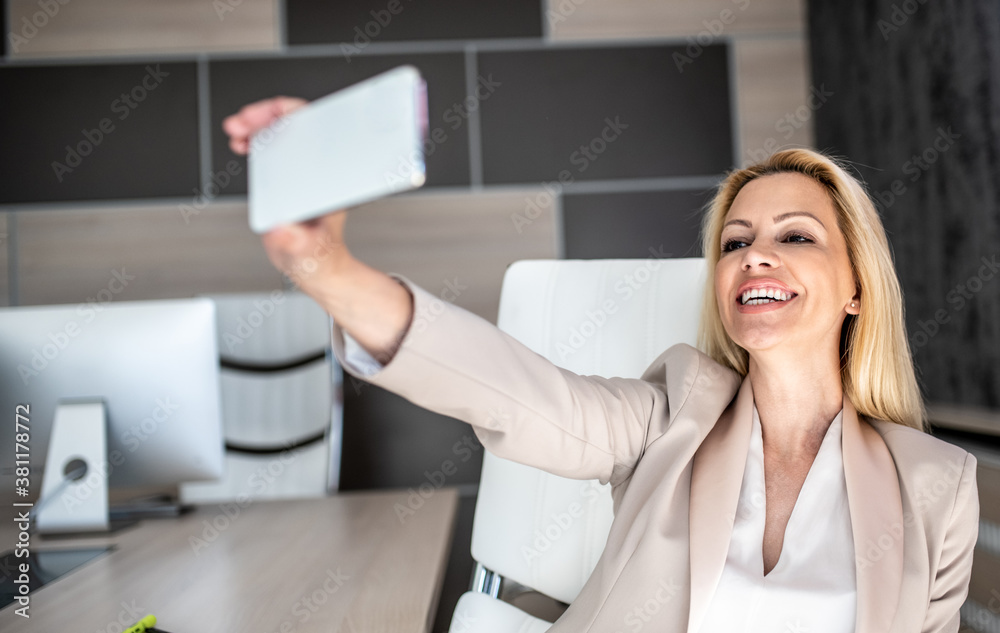 Fototapeta premium A business woman is sitting in her office and taking a selfie photo