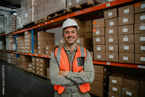 Smiling male worker standing cross-armed happily besides packaged parcels ready for delivery 