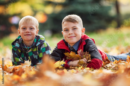 Smiling boys 6 and 10 years old lie on the ground in autumn leaves. Soft focus.