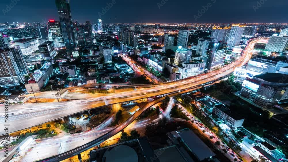 Time-lapse of car traffic transportation on highway road, toll gate at night. Cityscape view with construction crane on building. Urban transport lifestyle, Asian city life. High angle view, zoom out